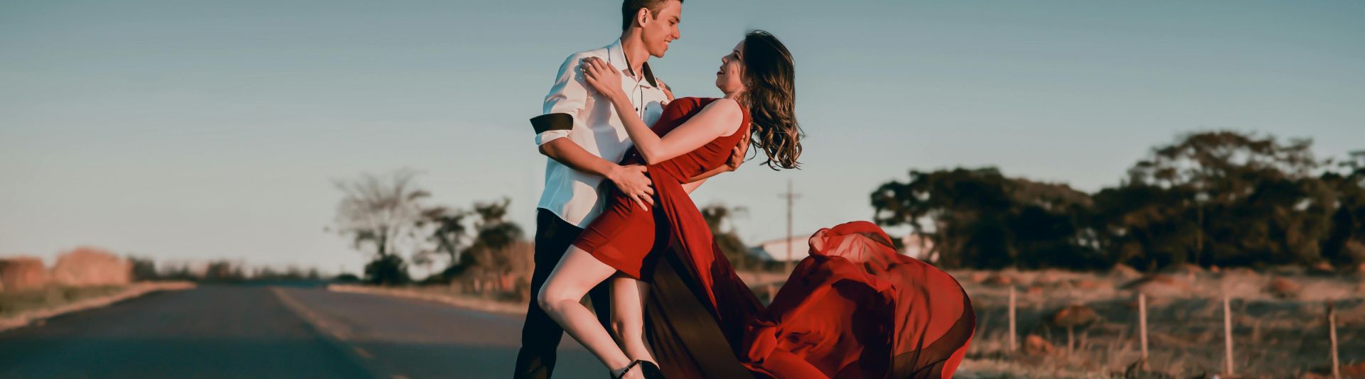 A couple in a passionate dance pose on an empty highway at sunset, showcasing love and romance.