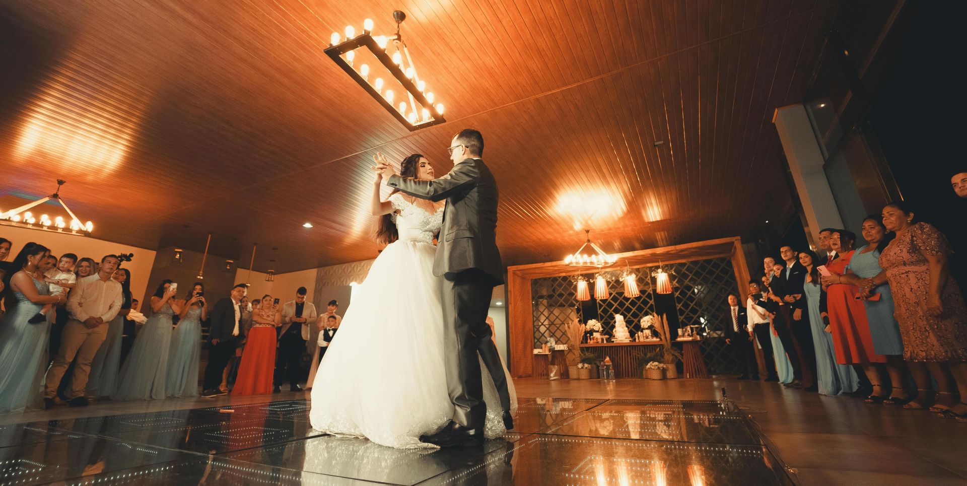 Bride and groom share a magical first dance surrounded by guests at a wedding reception.